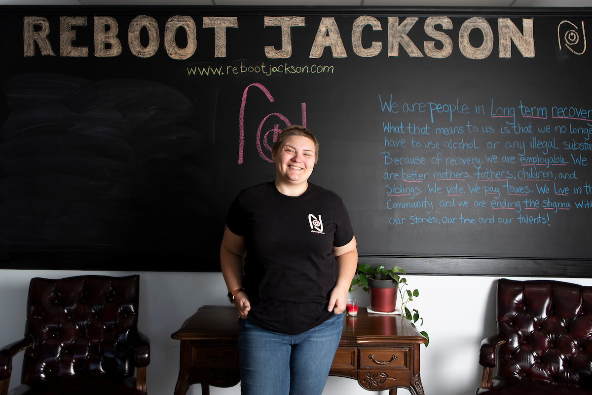 Woman stands in front of chalkboard with Reboot Jackson information on it.