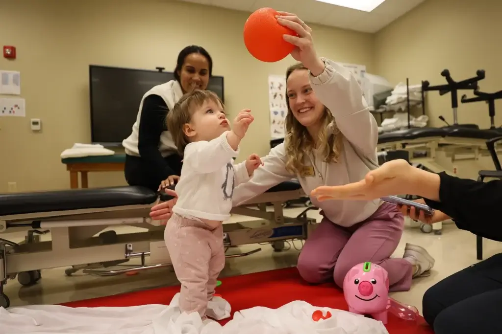 Occupational therapy students work with young child and mother assessing skills with red ball