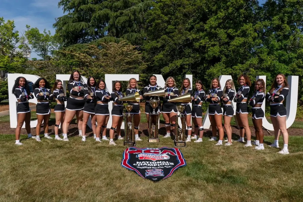 Brenau Cheer Team poses with trophy and banner in front of large Brenau letters outside