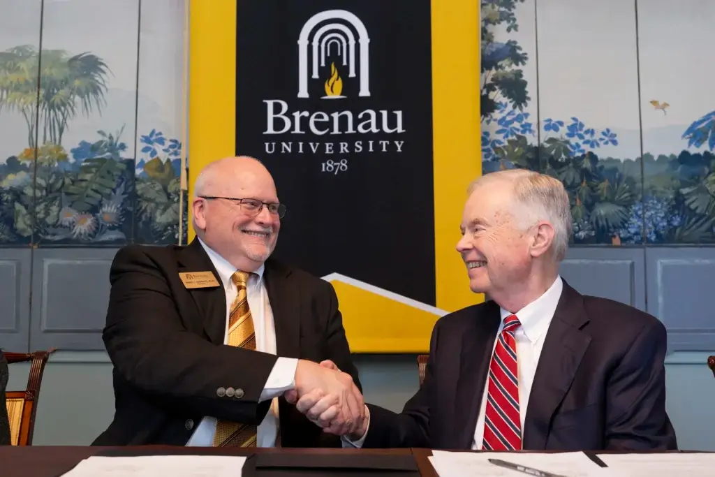 Presidents from Brenau and North Georgia Tech shake hands at table upon signing an articulation agreement.