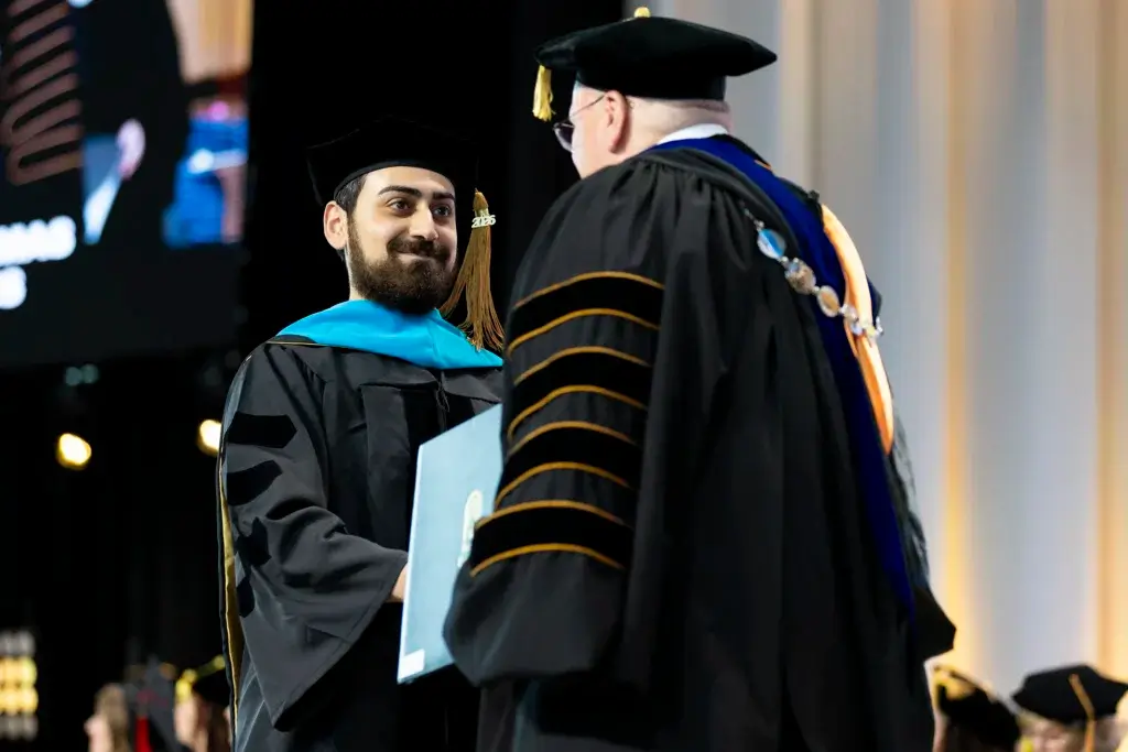 Graduating doctoral student shakes President Barnett's hand while receiving diploma at commencement